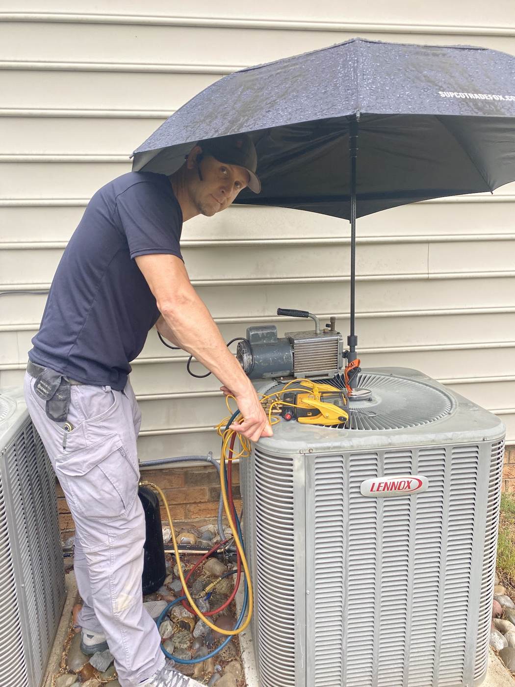 Technician servicing a residential AC condenser in the shade on a hot day